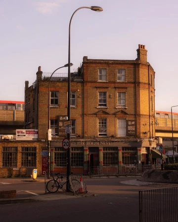 Exterior view of The Birds Nest pub in London, England, featuring its brick facade, street lamp, and bicycle parked nearby on a sunny day.
