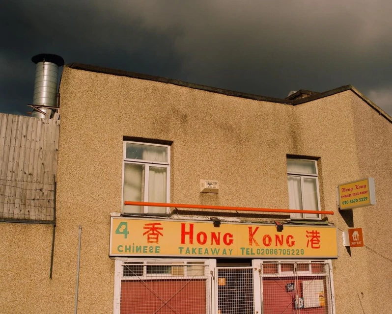 Exterior of Hong Kong Chinese takeaway restaurant on a cloudy day. Architectural details and signage visible. Street scene.