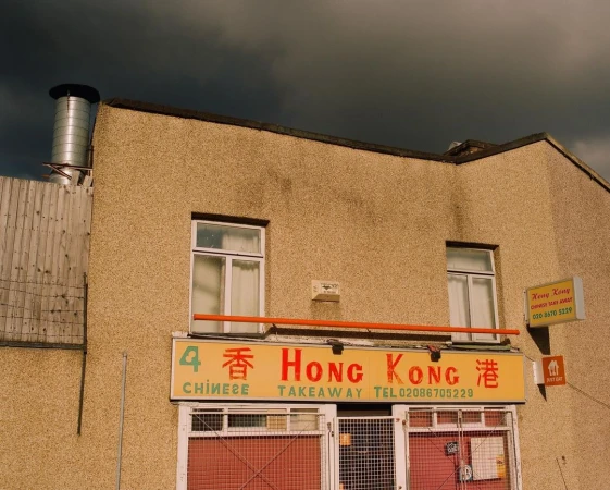 Exterior of Hong Kong Chinese takeaway restaurant on a cloudy day. Architectural details and signage visible. Street scene.