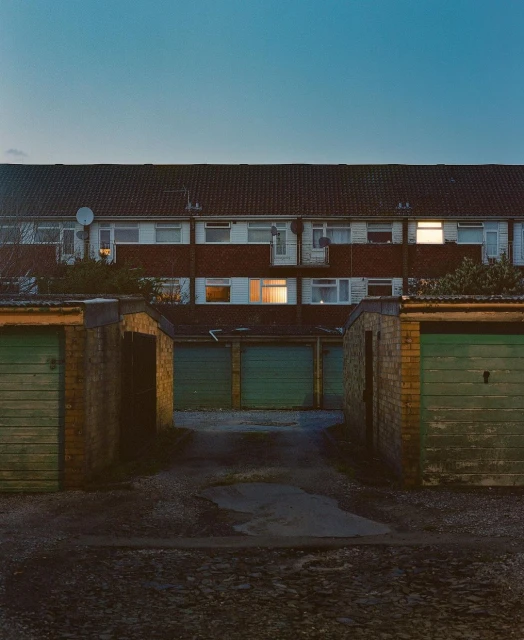 Exterior view of a row of brick apartments with garages, captured at night with lights glowing in the windows of some units.