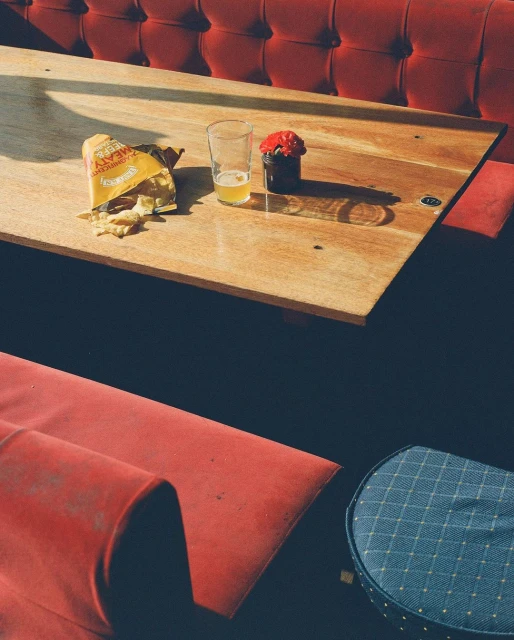 Still life of snacks and a drink on a wooden table next to red upholstered booth seating, with warm lighting and inviting atmosphere.