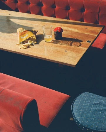 Still life of snacks and a drink on a wooden table next to red upholstered booth seating, with warm lighting and inviting atmosphere.