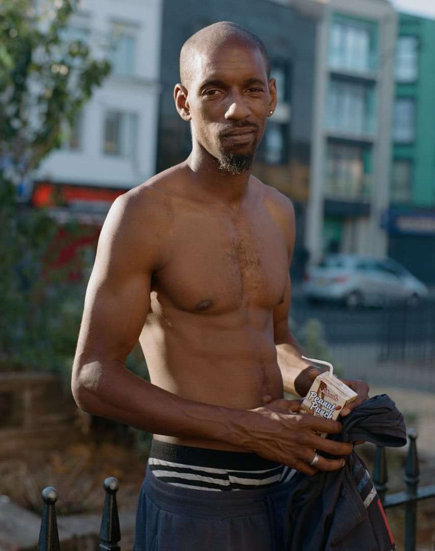 Shirtless black man holding a small carton with a straw on a London street by photographer Nico Froehlich.