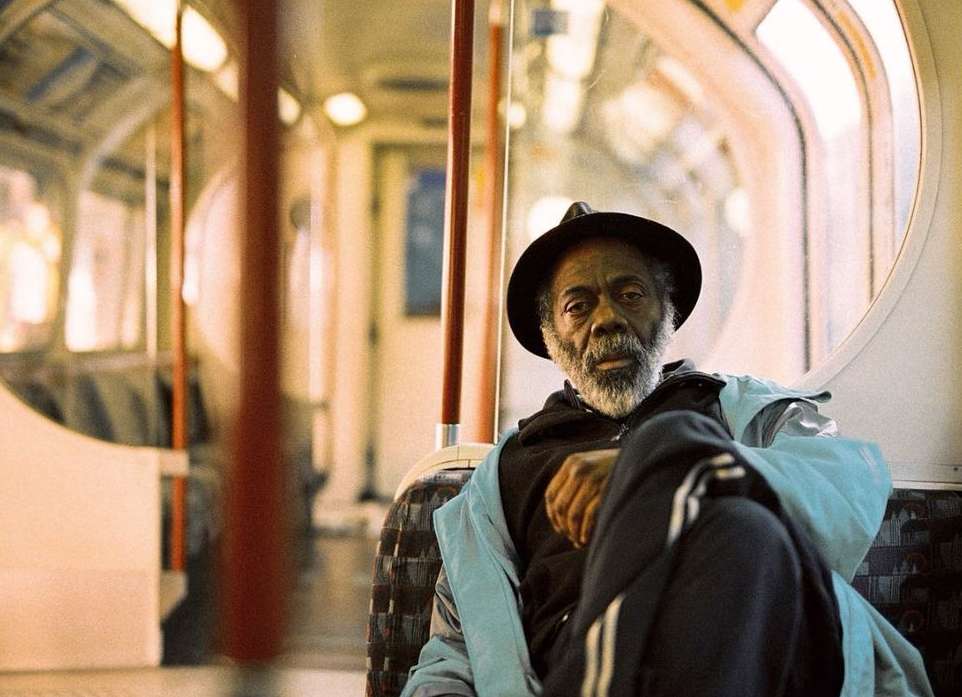 Older African-American man wearing a hat, seated in a subway car. He is wearing a blue jacket and is looking at the camera.