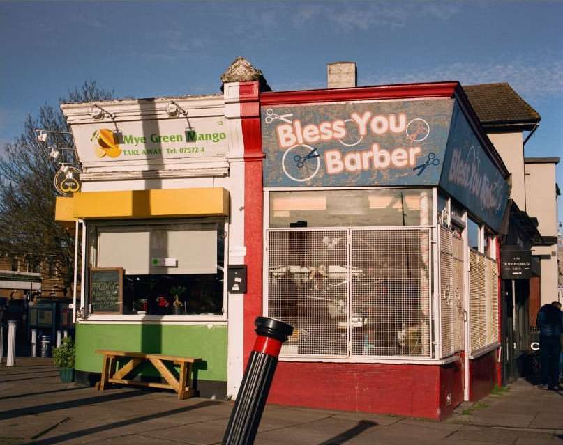 Street view of Mye Green Mango takeaway shop and Bless You Barber with exterior painted in red, white, yellow, green, and blue.