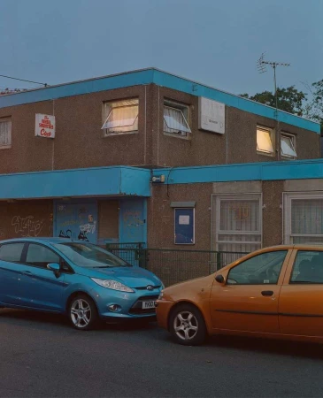Two cars parked in front of an older apartment building with blue trim, captured during an overcast day with muted lighting.