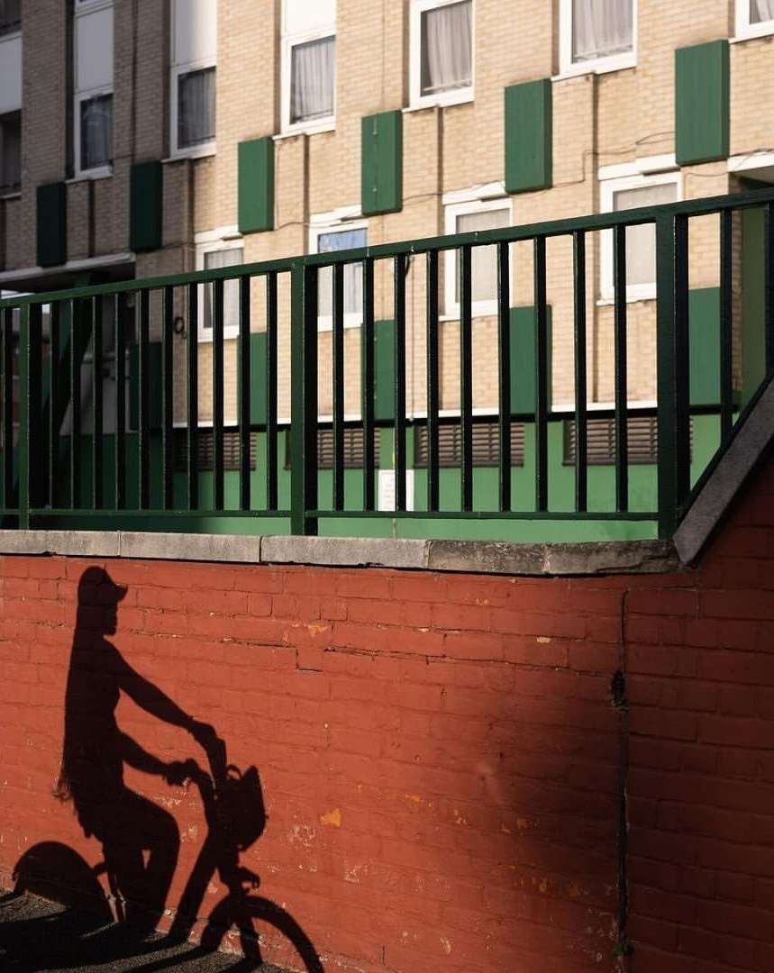 Silhouette of a person riding a bike projected onto a brick wall with an apartment building and green metal railing in the background.