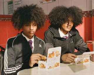 Two black teenage boys with long afros sitting at a table eating fried chicken from takeout boxes, photographed by Nico Froehlich.