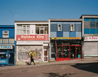 A person walking past storefronts with graffiti on a sloping street in London, captured by photographer Nico Froehlich.