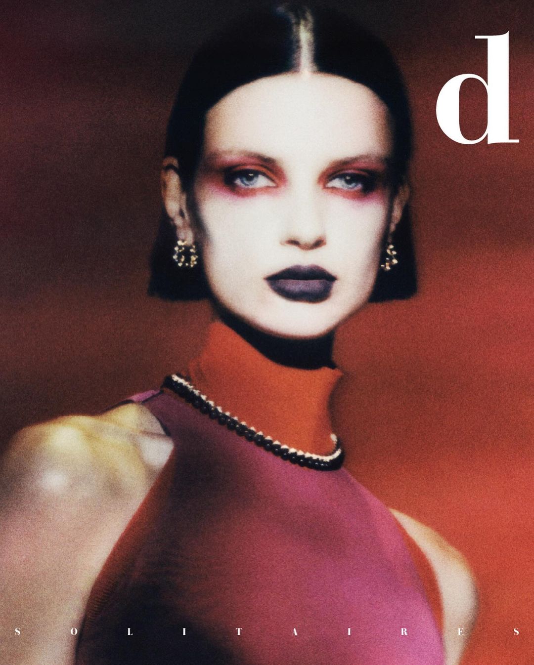 Fashion editorial portrait of a fair-skinned adult female model with dramatic makeup, wearing a red dress against a dark background.