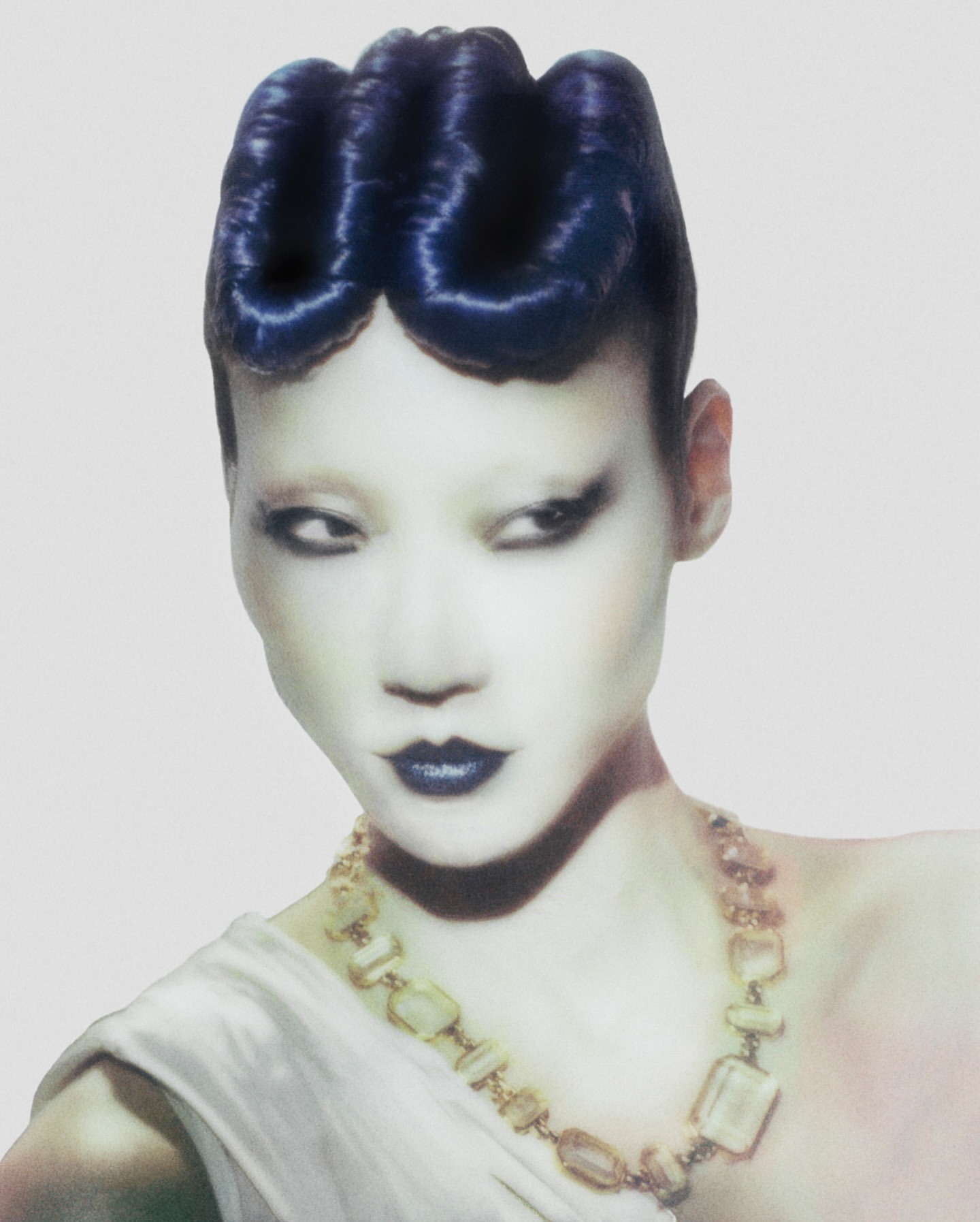 Fashion portrait of a person with blue hair and a necklace, featuring a white dress against a plain background in a studio setting.