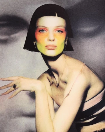 Model with short black bob and vibrant multi-coloured face makeup posing in front of a textured black and white background