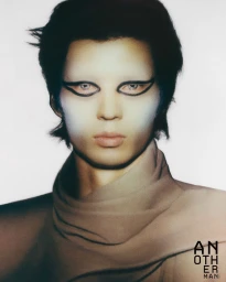 Portrait of a model with dark hair, dramatic black graphic eyeliner, and bleached eyebrows wearing a beige turtleneck.