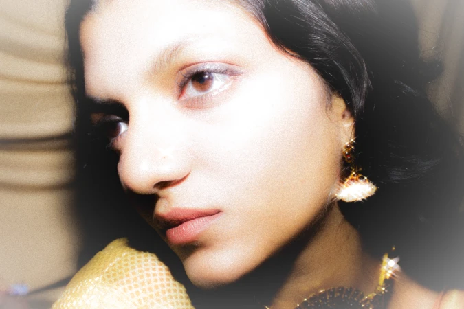 Close-up portrait of a woman with dark hair, wearing dangling gold earrings, looking away from the camera in soft, dreamlike lighting.