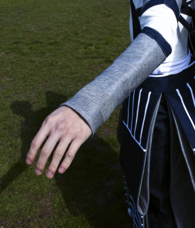 Close-up of a person's hand wearing a metallic silver fabric sleeve, paired with a black and white geometric skirt on a grassy field.