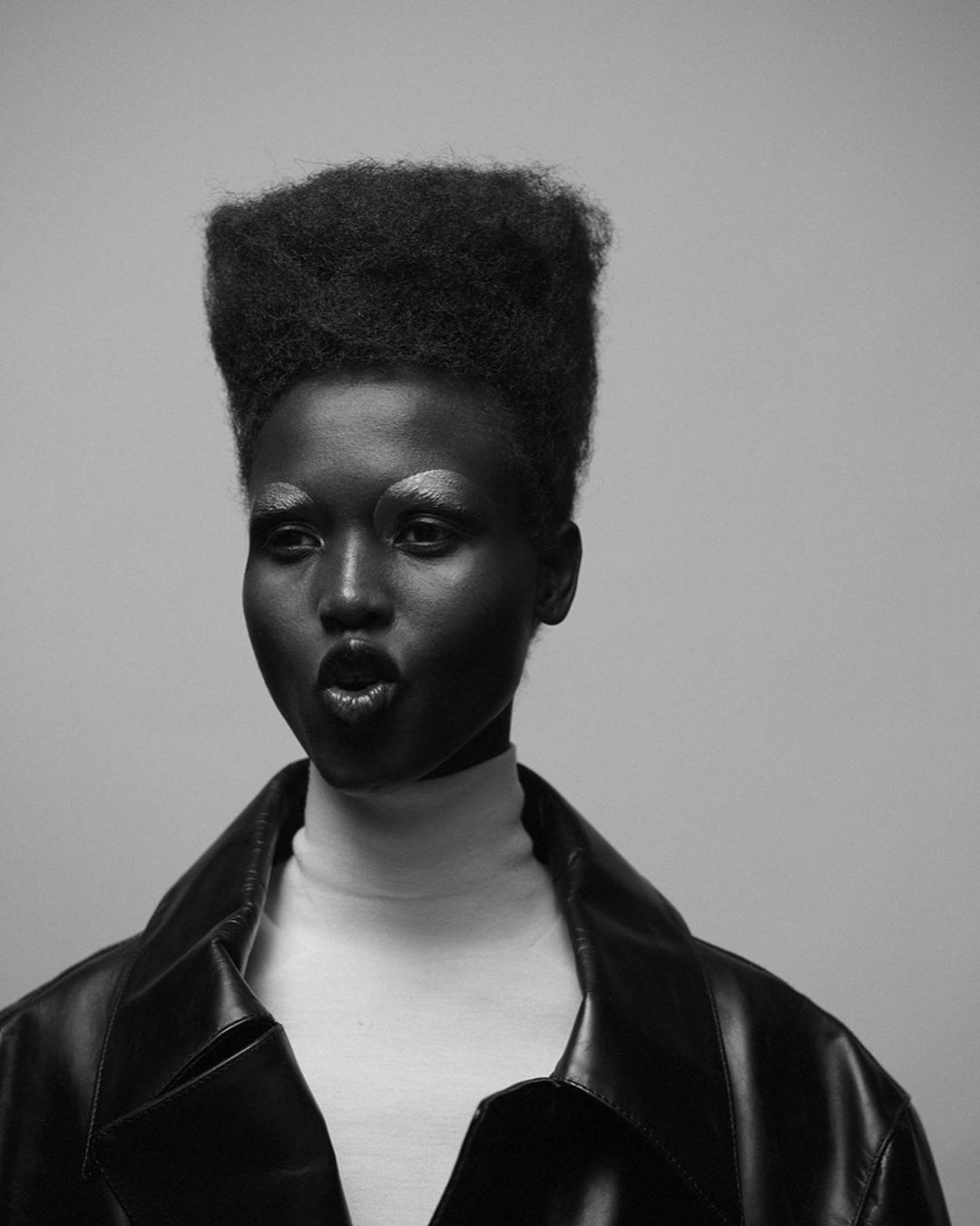 Monochrome portrait of a woman with dark skin and a large afro wearing a black leather jacket and making a kiss face.