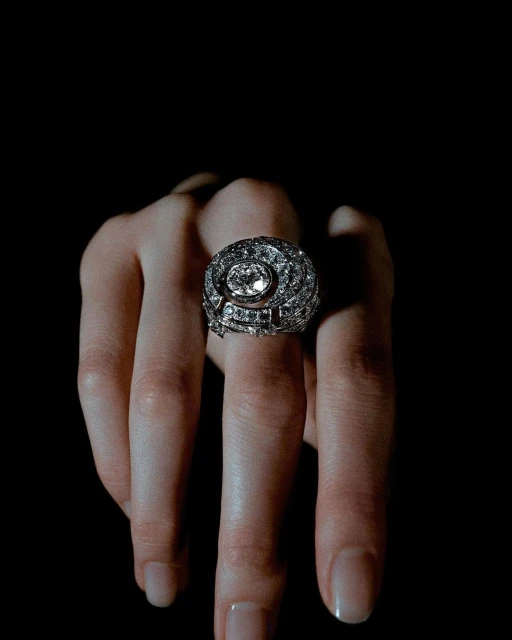 Close-up of a woman's fingers wearing an ornate diamond ring against a dark background, emphasizing its luxury and craftsmanship.
