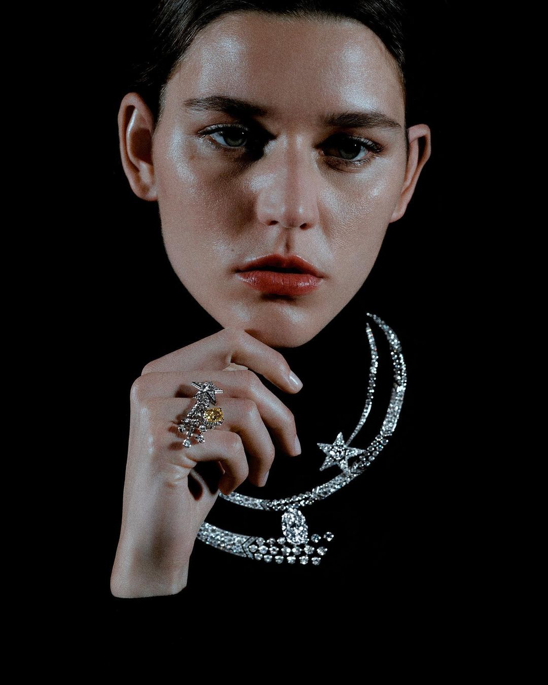 Woman with fair skin poses against a black background wearing a diamond necklace and ring, studio lighting, beauty shot, head and shoulders.