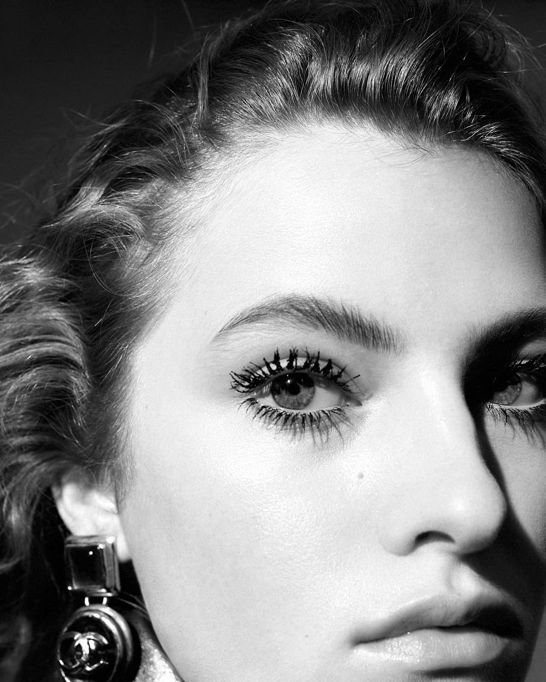 Close-up portrait of a woman with dark wavy hair wearing statement earrings and dramatic mascara by photographer Nicolas Kantor.
