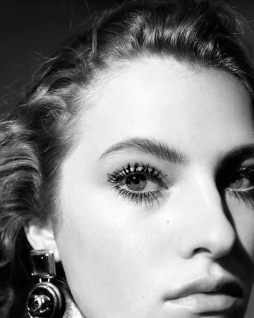 Close-up portrait of a woman with dark wavy hair wearing statement earrings and dramatic mascara by photographer Nicolas Kantor.