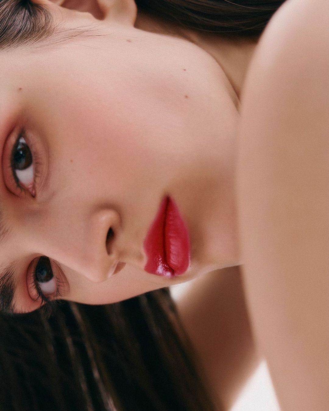 Close-up portrait of a woman with dark hair and red lipstick, fair skin, light pink eye shadow, looking at the camera, beauty shot.