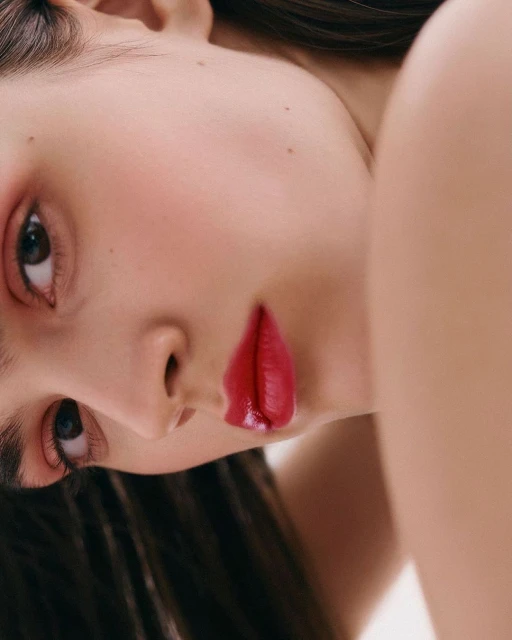 Close-up portrait of a woman with dark hair and red lipstick, fair skin, light pink eye shadow, looking at the camera, beauty shot.