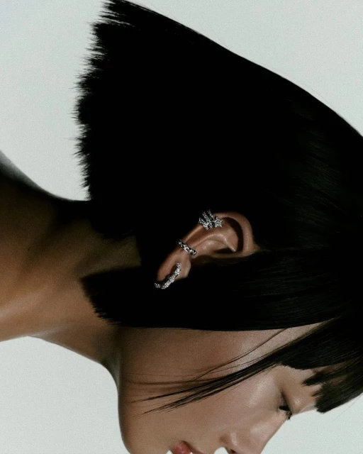 Close-up shot of a person with dark hair wearing multiple ear cuffs on their left ear, set against a bright, neutral background.