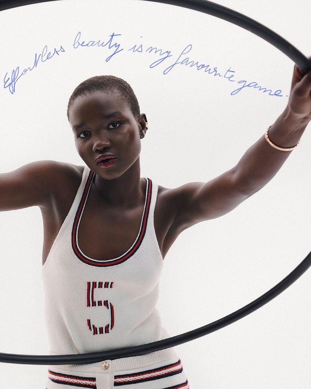 Portrait of a woman wearing a tank top with the number '5' on it, posing with a hula hoop in front of a white background.
