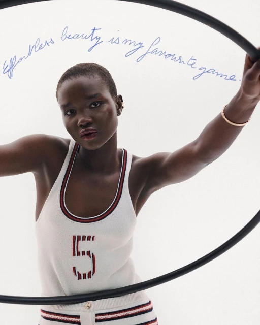 Portrait of a woman wearing a tank top with the number '5' on it, posing with a hula hoop in front of a white background.
