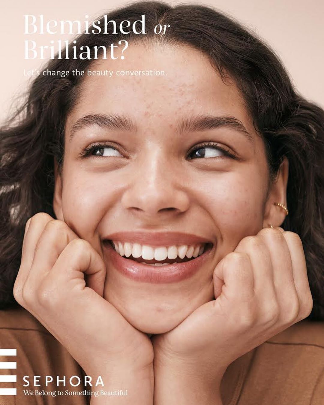 Close-up portrait of a smiling young woman with natural skin texture, soft lighting, and a Sephora logo in the foreground, beauty advertising.