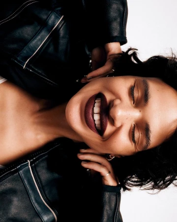 Close-up portrait of a smiling woman with dark hair wearing a black leather jacket against a white background