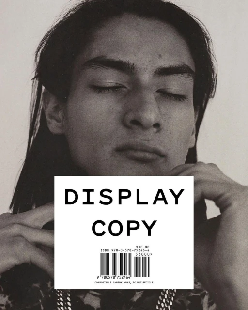 Portrait of a young adult with long dark hair and closed eyes, partially covered by a block of white paper with 'Display Copy' on it.