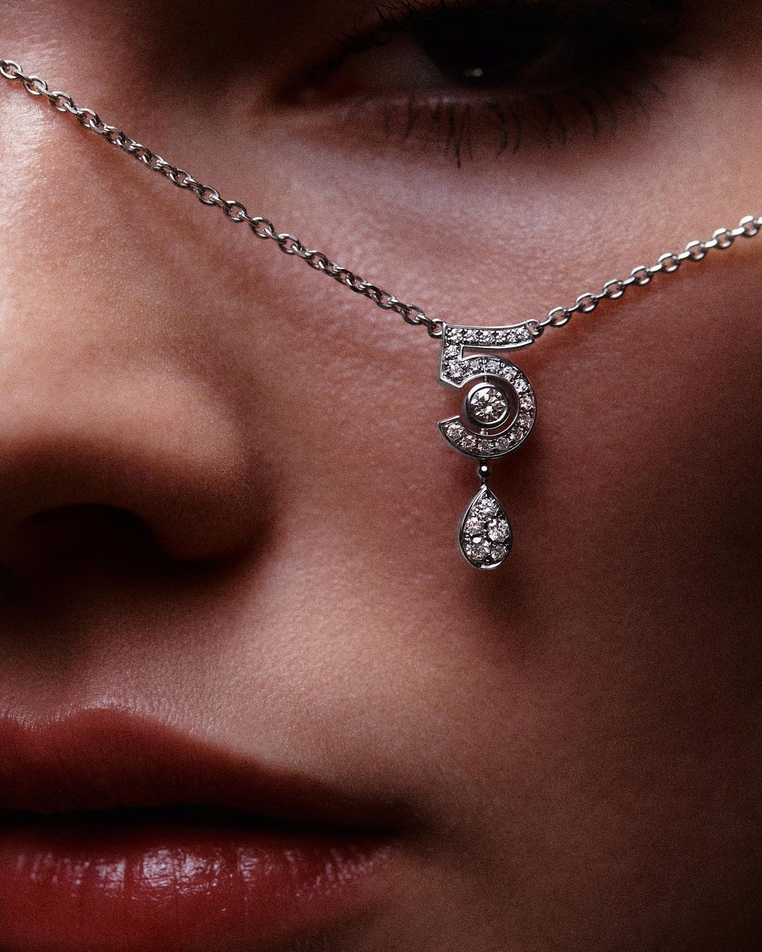Close-up of a fair-skinned person wearing a delicate silver necklace featuring a diamond-studded '5' pendant, showcasing beauty and jewelry.
