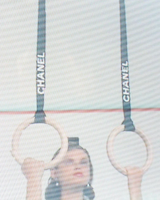 Woman performs on gymnastic rings in a fashion photoshoot. The logo for Chanel is visible on the black ring straps.