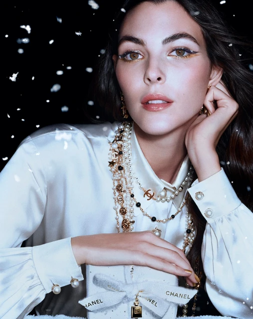 Close-up of a woman wearing jewelry and holding a Chanel gift box with falling snow in the background. Beauty shot for fashion.