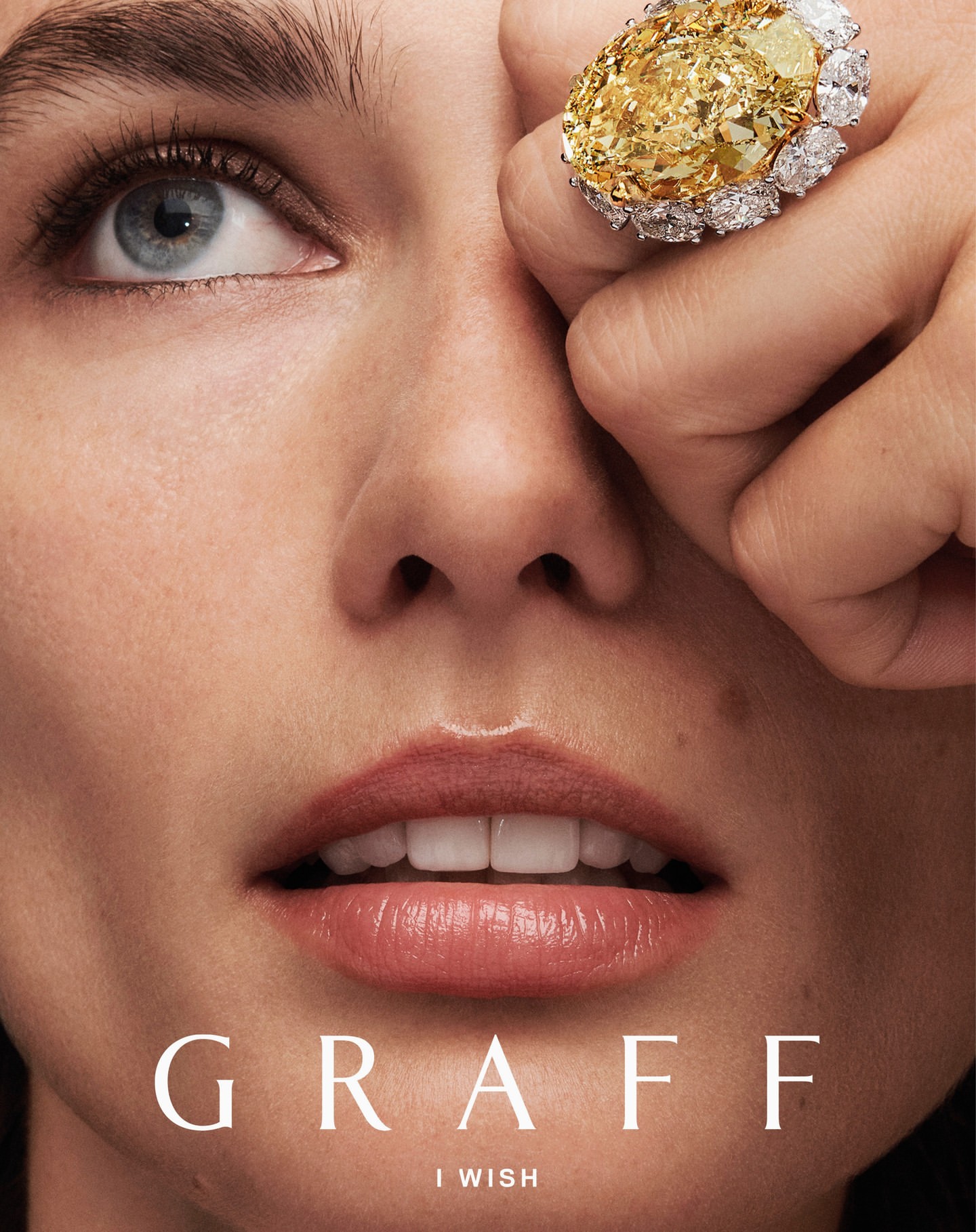 Close-up beauty shot of a fair-skinned female with light blue eyes wearing yellow diamond jewelry from GRAFF jewelry collection.