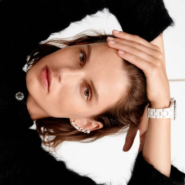 Close-up portrait of a woman with brown hair and fair skin wearing a black sweater, with an ear cuff and a white watch.