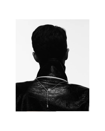 Rear view of a man wearing a black leather jacket and a delicate silver necklace against a stark white background.
