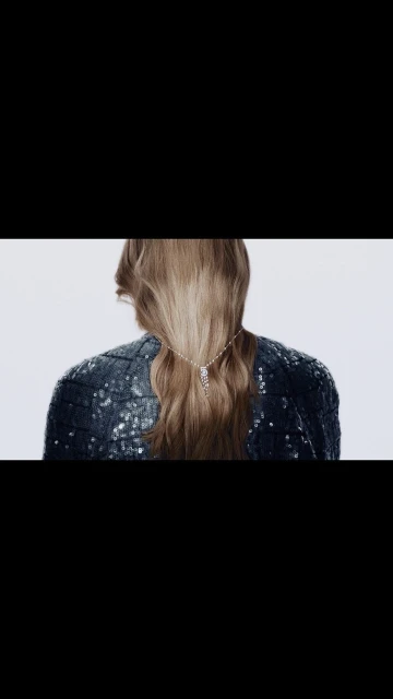 Blonde woman with a rhinestone hair clip in a sequined blazer on a white backdrop, presented from the back.
