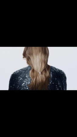 Blonde woman with a rhinestone hair clip in a sequined blazer on a white backdrop, presented from the back.