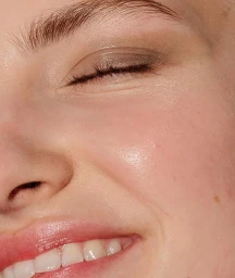 Extreme close-up portrait of a smiling woman with closed eyes, showing subtle eyeshadow and glossy lips photographed by Nicolas Kantor