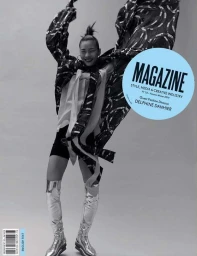 Model in silver boots and patterned coat jumping with arms raised against a plain studio background
