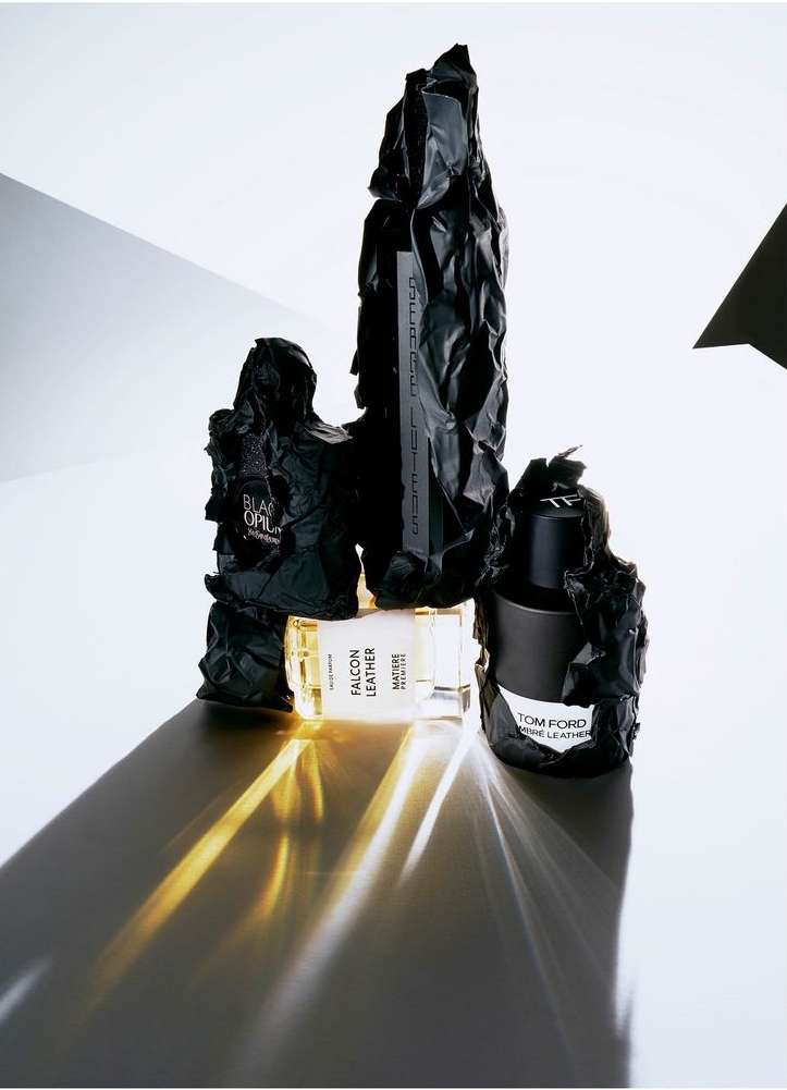 A group of perfume bottles with dark, textured wrapping, set against a white background with geometric shapes, with shadows.