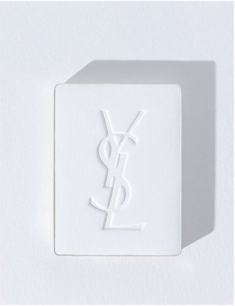 Elegant, minimalist close-up of a white cosmetic compact case featuring a debossed YSL logo on a white background and soft shadows.