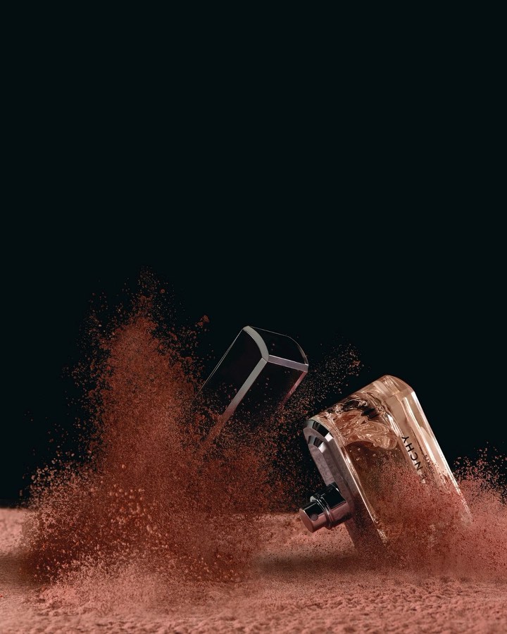 Still life of two Givenchy perfume bottles, one with the cap off, surrounded by brown powder against a black background in a studio setting.