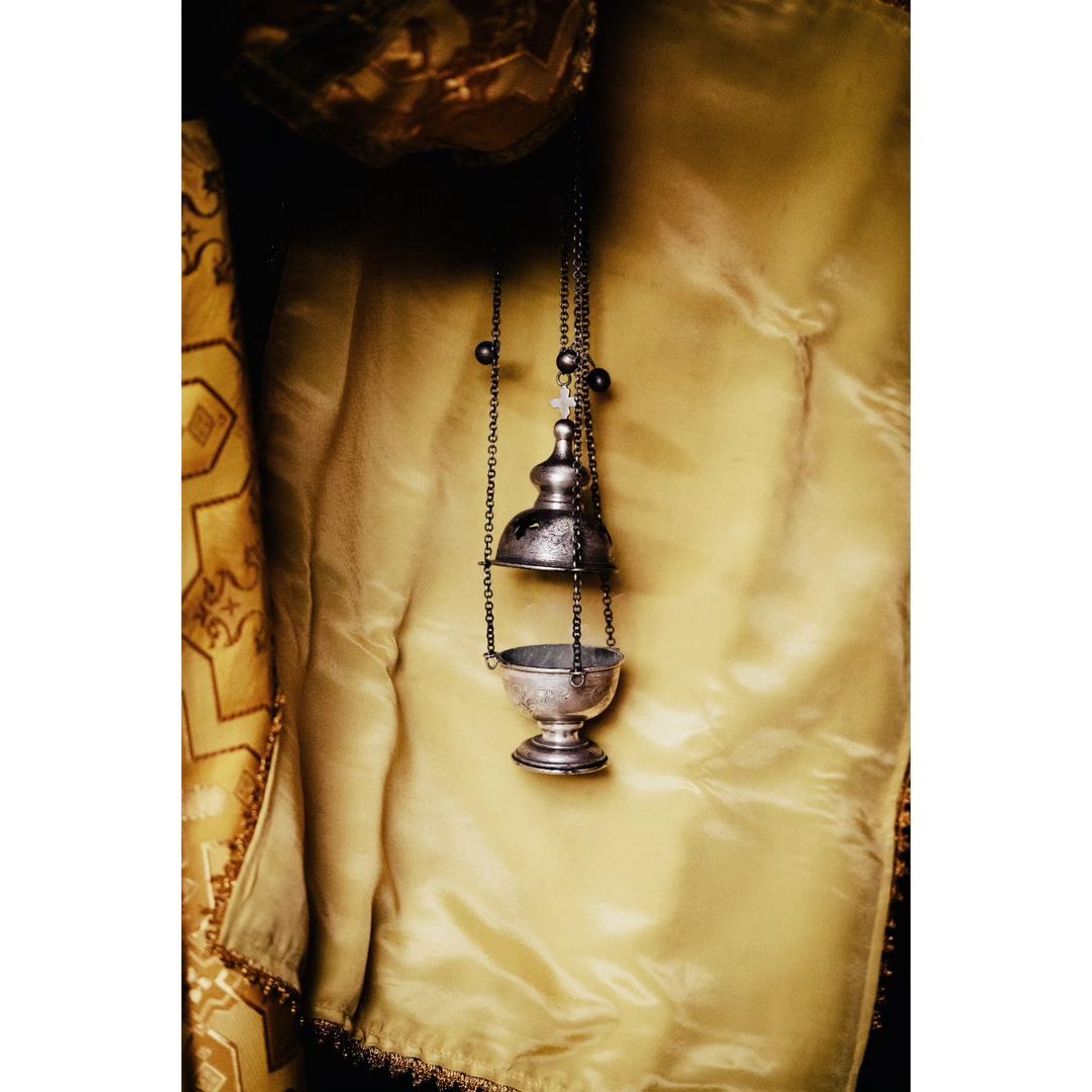Close-up studio shot of an incense burner suspended by chains against a gold fabric backdrop, showcasing its intricate design and materials.
