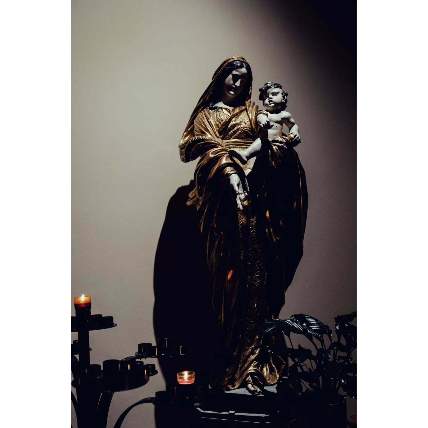 Golden statue of Virgin Mary holding baby Jesus, illuminated by candlelight in a dark room, evoking religious symbolism.