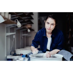 Woman in blue shirt shaping clay on a potter wheel in a studio by Nicolas Lascourrèges