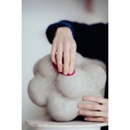 Close-up of hands shaping a lumpy ceramic sculpture with a red tool in Paris by Nicolas Lascourrèges
