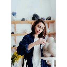 Woman in blue corduroy shirt and white t-shirt shaping a clay sculpture in a studio by Nicolas Lascourrèges
